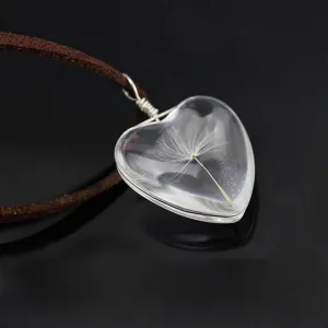 Close-up detail of a clear glass heart pendant necklace featuring a real natural dandelion seed.