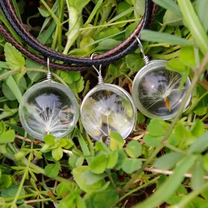 Close-up detail of a handmade dandelion seed glass ball pendant necklace in a natural grass.