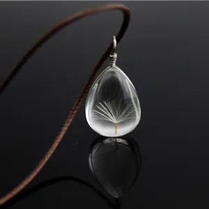 Close-up detail of a transparent teardrop glass pendant necklace featuring a real dandelion seed.