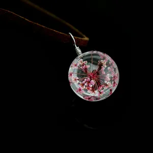 Close-up detail of a clear glass ball pendant featuring delicate dried pink flowers and cord.