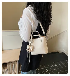 Detail shot of a white faux leather bucket tote bag with cute bear charm for daily commute.