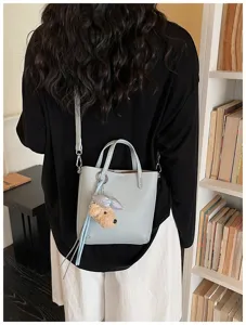 Minimalist leather bucket bag with cute plush dog charm, stylish daily commuter handbag.