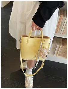 Detailed view of the yellow leather tote bag with cute plush charm and shoulder strap.