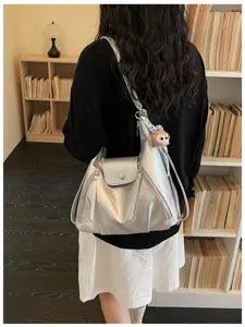 Detail shot of stylish metallic silver women shoulder backpack with dual zippers and cute pendant.