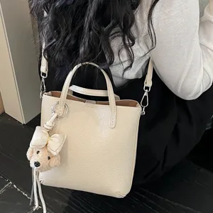 Beige leather tote bag for women, stylish crossbody shoulder bag with cute fluffy bear pendant.