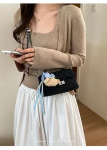 Dettaglio chic di borsa a tracolla trapuntata nera con ciondolo orsetto di peluche.