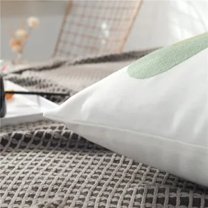 Close-up detail of white throw pillow with green embroidery in cozy home setting.