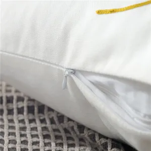 Close-up detail of white canvas pillow cover with hidden zipper and yellow embroidery.