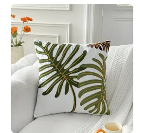 Detailed view of Nordic style embroidered leaf cushion on textured white sofa in bright room.