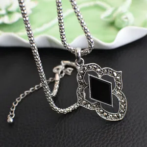 Close-up of vintage Thai silver pendant necklace with black rhombus stone and delicate chain.