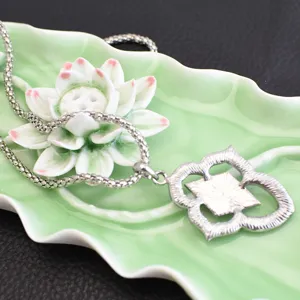 Detailed view of silver quatrefoil pendant necklace on lotus dish, elegant retro design.