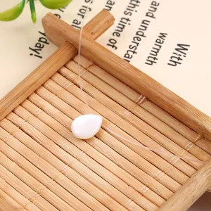 Closeup detail of the minimalist teardrop shell pearl necklace on wooden tray display.