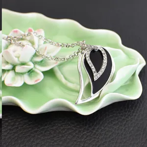 Detailed close-up of a stylish rhinestone teardrop pendant necklace resting on a lotus ceramic dish.