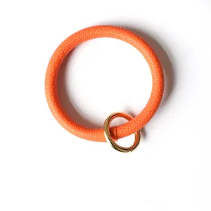 Detailopname van de helderoranje PU-lederen ronde armband-sleutelhanger met gouden ring.
