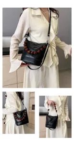 Detailed view of black bucket bag with amber beaded handle, worn on shoulder by model.