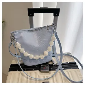 Detail view of light blue bucket bag with white pearl beaded handle and crossbody strap.