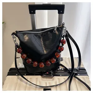 Detailed view of women's black bucket handbag featuring handmade amber bead strap and shoulder strap.