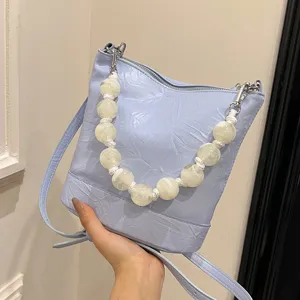 Light blue bucket bag for women featuring handmade white beaded handle, stylish crossbody design.
