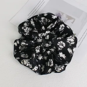 Detailed close-up of a chic black and white floral hair scrunchie, soft elastic fabric.