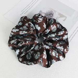 Detailed close-up of brown floral satin hair scrunchie, soft texture, elegant accessory.