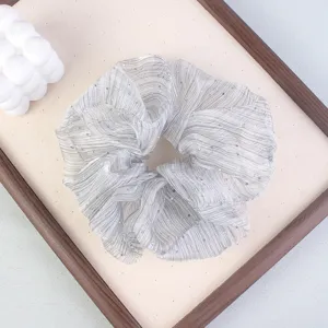 Close-up detail of a grey sheer scrunchie with subtle shimmer dots on a wood tray.