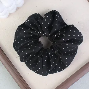 Close-up view of a black hair scrunchie with white polka dots, featuring smooth fabric texture.