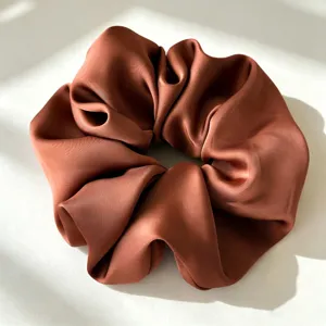 Close-up van de satijnen haarelastiek met gladde bruine stof en elegant geplooid ontwerp.