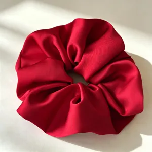 Detailweergave van levendig rode satijnen scrunchie, met gladde textuur en elegant haaraccessoire.