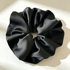 Gedetailleerde close-up van een elegante zwarte satijnen haarscrunchie met gladde textuur.
