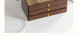 Wooden jewelry box detail view showing walnut grain finish, transparent lid and gold knobs.