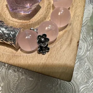 Close-up detail of pink quartz beaded jewelry with silver flower charm on wood tray.