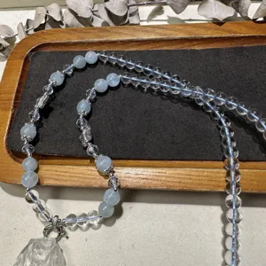 Detail view of handcrafted crystal fox pendant necklace with clear and blue bead strands on tray.