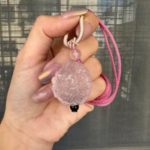 Gros plan détaillé du pendentif en cristal de quartz rose sculpté avec cordon tressé rose.