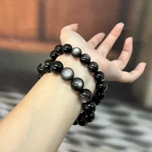 Detail shot of natural silver obsidian beaded bracelets on wrist, showing strong cat eye sheen.
