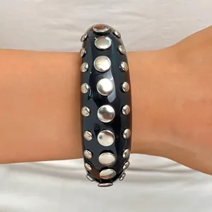 Close-up detail of wide black resin statement bangle featuring silver tone metal stud embellishments.