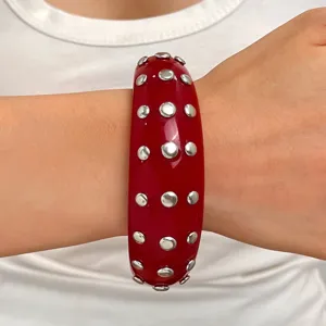 Detailed shot of a wide red resin cuff bracelet featuring double rows of silver-toned metal studs.
