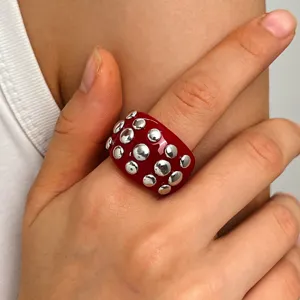 Close-up detail of punk style wide resin ring with red amber finish and metallic studs.