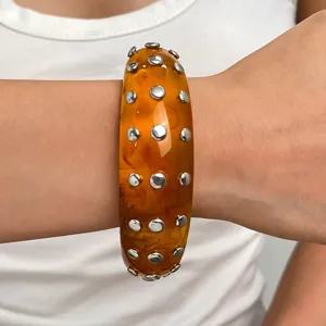 Close-up detail of the amber resin wide bangle bracelet featuring double rows of silver metal studs.