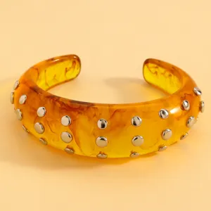 Amber resin cuff bracelet detail showing double rows of metallic studs on glossy surface.