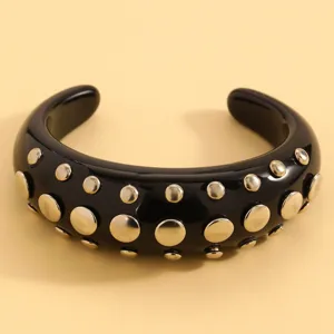 Close-up of black resin cuff bracelet with gold-tone studs, punk style fashion jewelry detail.