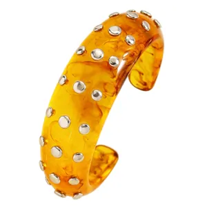 Amber resin cuff bracelet detail showing double rows of metallic studs and unique pattern.