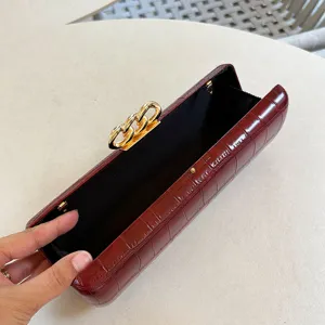 Close-up of burgundy crocodile pattern clutch bag interior and gold chain clasp detail.
