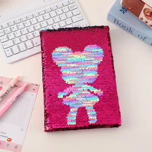 Detailed view of a vibrant pink reversible sequin notebook with a cute rainbow cartoon pattern.