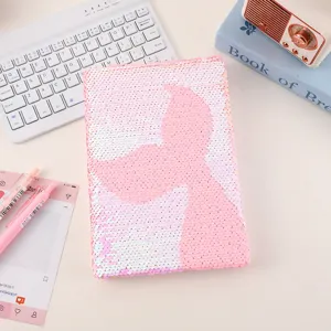 Close-up detail of the pink reversible sequin notebook with mermaid tail pattern on desk.