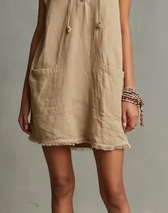 Close-up view of the sleeveless beige mini dress featuring front pockets and frayed hem details.