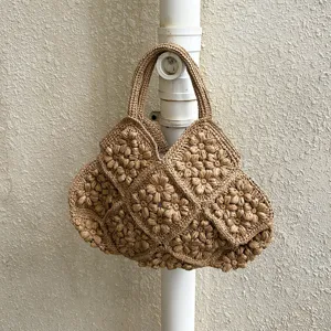 Handgemachte florale Stroh-Totetasche Detail, mit exquisiten 3D-Häkelblumen und beigem Farbton.