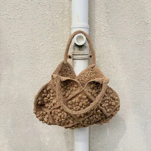 Detailansicht der handgehäkelten Strohtasche mit 3D-Blumenmuster in einer ländlichen Szene.