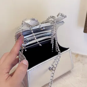 Nahaufnahme einer silbernen Metallic-Mini-Abendtasche mit funkelnden Strass-Schleifen und Kettchen.