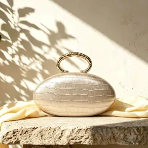 Elegant oval clutch bag detail, gold textured metal ring handle, chic evening accessory.