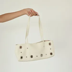Close-up detail of beige leather shoulder tote bag featuring metallic eyelet rings and stud accents.